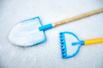 A toy spade and rake left outside on a tale in the snow.