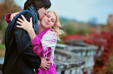Love story of young beautiful couple in Peterhof, Saint-Petersburg, Russia at autumn. Blonde girl in pink coat and blue dress and man or groom in black jacket and jeans. Embrace kiss with fall in love