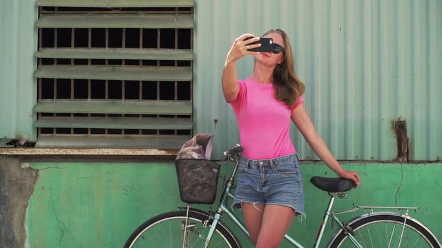 Girl make photo on phone with bicycle stand near old wall rapid slow motion