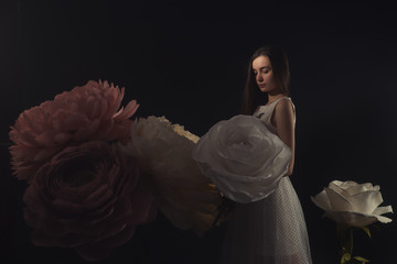 girl in a light dress among the huge flowers made of paper and formina