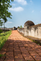 Madikeri, India - October 31, 2013: Walkway and defensive wall on top of ramparts of fort. Red stones as tiles. Green vegetation. Gray wall. Blue sky.