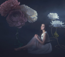 girl in a light dress among the huge flowers made of paper and formina