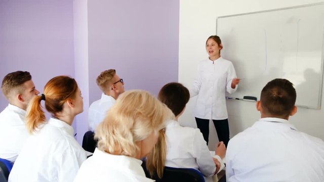 Male medical student answering near whiteboard in front of teacher and group of students in auditorium