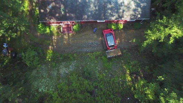 As a skid steer loader turns around with a bucket full of dirt, the aerial camera flies straight up to give a broader picture of the natural surroundings.