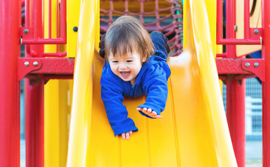 Mixed race toddler boy playing on a slide at a playground