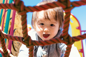 Multracial toddler boy climbing on a playground ropes