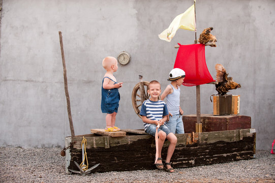 Three cute boys on a pirate ship as sailors on summer evening. Children have fun outdoors. Happy kids on holiday in village. Home show with an vintage boat and a white chicken. Adventures are going