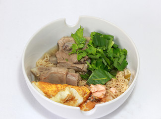 Boiled instant noodles with pork rip, fried egg, fish meat and green vegetable in the white bowl. Simple cooking at home.