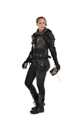 full length portrait of female  soldier wearing black  tactical armour, holding a remote control, isolated on white studio background.