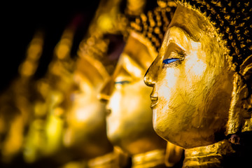 Close-up of statues of golden buddha faces in a Thai temple
