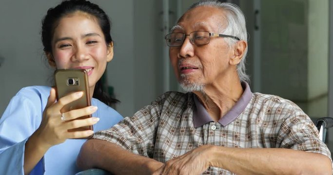 Elderly Asian man sitting on wheelchair and taking selfie photo with his nurse in hospital. Shot in 4k resolution