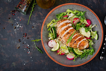 Bowl with salad of fresh vegetables and baked chicken breast on a dark background. Proper...