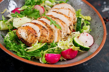 Bowl with salad of fresh vegetables and baked chicken breast on a dark background. Proper nutrition. Dietary menu.