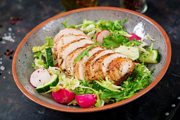 Bowl with salad of fresh vegetables and baked chicken breast on a dark background. Proper nutrition. Dietary menu.