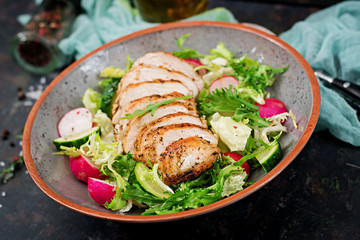 Bowl with salad of fresh vegetables and baked chicken breast on a dark background. Proper nutrition. Dietary menu.