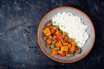 Chicken hearts with pumpkin and tomatoes in tomato sauce. The garnish is served with boiled rice. Flat lay. Top view.