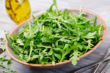 Fresh leaves of arugula in a bowl on a light wooden background