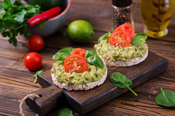 Healthy breakfast. Sandwich crisp bread with guacamole and tomatoes on a wooden background.