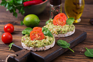 Healthy breakfast. Sandwich crisp bread with guacamole and tomatoes on a wooden background.