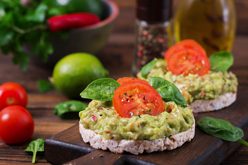 Healthy breakfast. Sandwich crisp bread with guacamole and tomatoes on a wooden background.