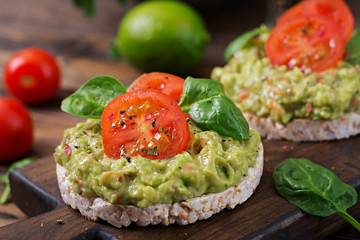 Healthy breakfast. Sandwich crisp bread with guacamole and tomatoes on a wooden background.
