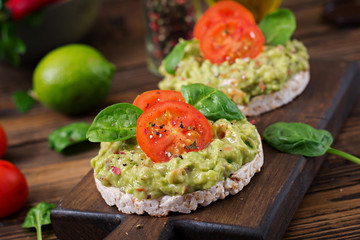Healthy breakfast. Sandwich crisp bread with guacamole and tomatoes on a wooden background.
