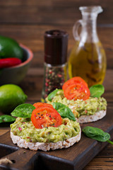 Healthy breakfast. Sandwich crisp bread with guacamole and tomatoes on a wooden background.