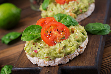 Healthy breakfast. Sandwich crisp bread with guacamole and tomatoes on a wooden background.