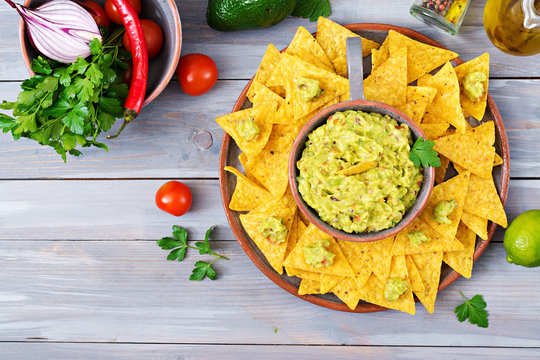 Guacamole avocado, lime, tomato, onion and cilantro, served with nachos - Traditional Mexican snack. Flat lay. Top view.