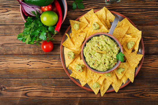 Guacamole avocado, lime, tomato, onion and cilantro, served with nachos - Traditional Mexican snack. Flat lay. Top view.