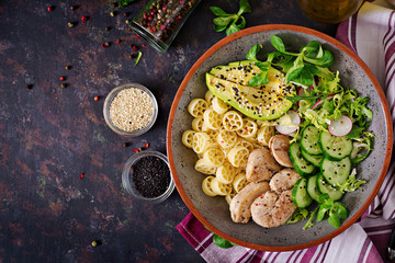 Healthy salad with chicken, avocado, cucumber, lettuce, radish  and pasta on dark background. Proper nutrition. Dietary menu. Dinner. Flat lay. Top view