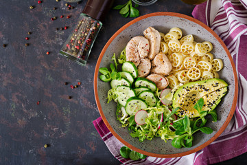 Healthy salad with chicken, avocado, cucumber, lettuce, radish  and pasta on dark background. Proper nutrition. Dietary menu. Dinner. Flat lay. Top view