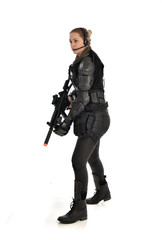full length portrait of female  soldier wearing black  tactical armour, holding a rifle gun, isolated on white studio background.