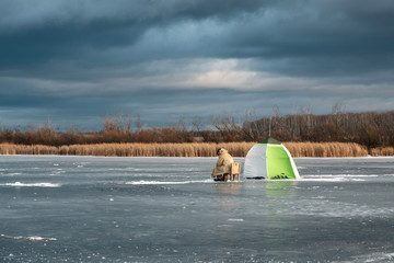 blue tragic sky ice on the pond and the fisherman sits near the scarf, winter period