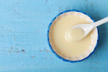 Condensed milk or evaporated milk in bowl on blue table top view. - Powered by Adobe