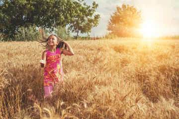 Naklejka na ściany i meble Happy little girl in a field of ripe wheat