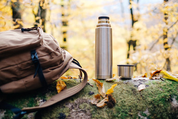 Backpack and thermos in autumn park.