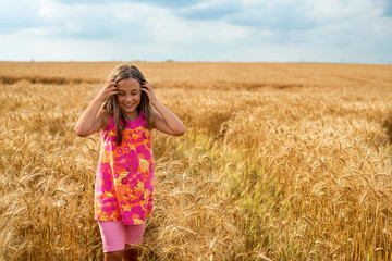 Happy little girl in a field of ripe wheat