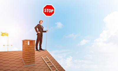 Caucasian businessman on brick house roof showing stop road sign. Mixed media