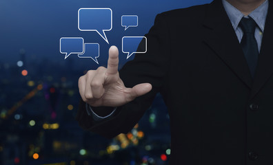Businessman point to social chat sign and speech bubbles over blur colorful night light city tower, Social network concept