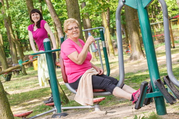Fototapeta na wymiar Senior and young woman exercising lower body on outdoor gym, healthy lifestyle concept
