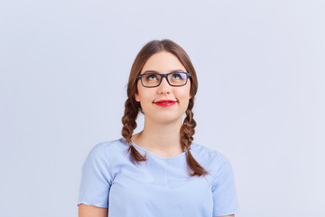 A young girl in pigtail glasses thinks, dreams with a positive emotion on a gray background.