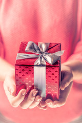 Female hands holding a red gift wrapped with silver ribbon.