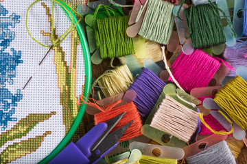 The process of cross-stitch. Canvas on hoops, needles, embroidery floss and pattern.