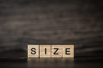 the word size consisting of a light wooden cubes on a dark wooden background
