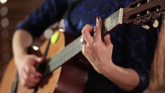 A girl in a blue dress is playing an acoustic guitar. Close-up. Hands on the strings of a musical instrument. Defocus at the end of the video.