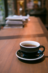 Hot coffee cup on wooden table with books background in vintage tone