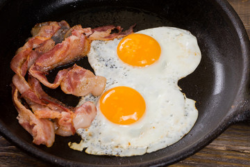 Bacon and Egg. Salted egg and sprinkled with black pepper. English breakfast. Grilled bacon, two eggs on pan on wooden table.