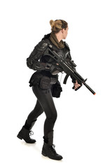 full length portrait of female  soldier wearing black  tactical armour, holding a rifle gun, isolated on white studio background.