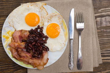 Plate with scrambled eggs, bacon and beans on a wooden rustic table.